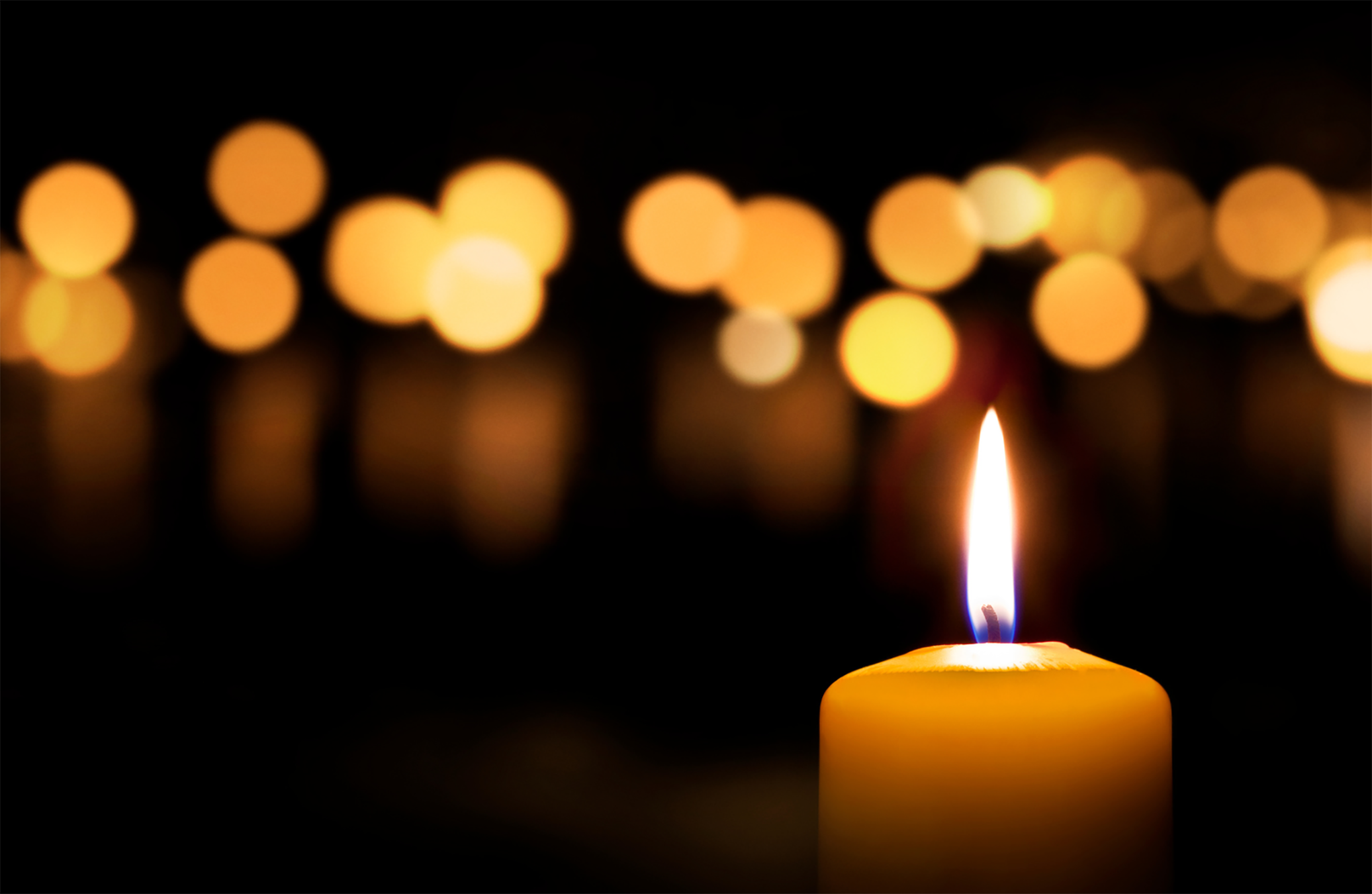 single lit candle in foreground with candlelight from multiple candles in background.